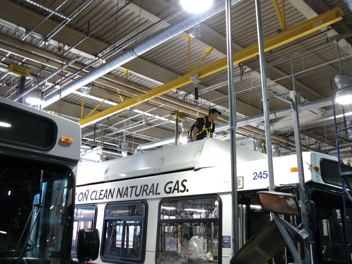 Worker using overhead fall protection for transit bus maintenance